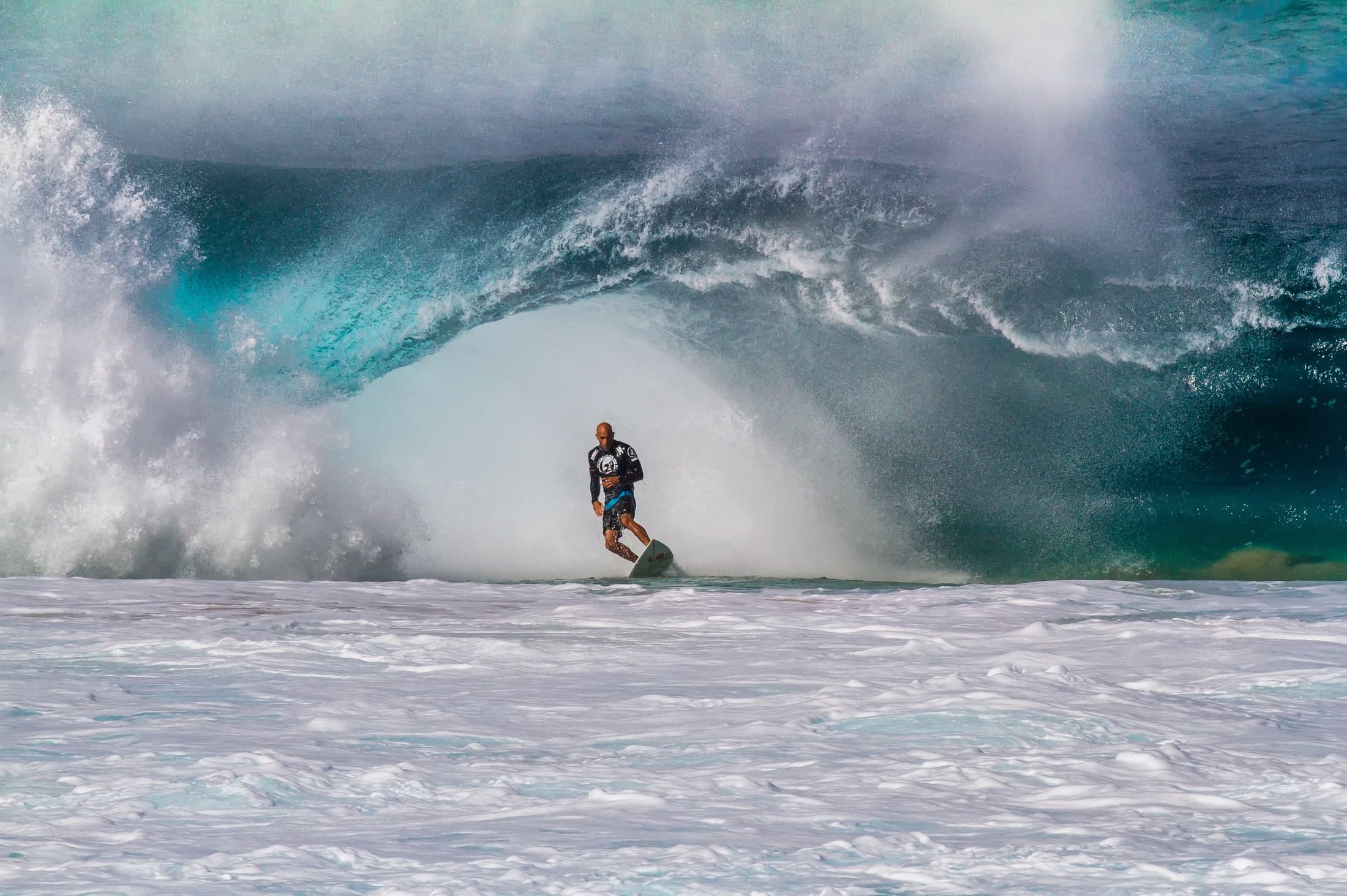 Kelly Slater emerging from a towering barrel at Pipeline, Hawaii. Photograph by Fosterand sons.